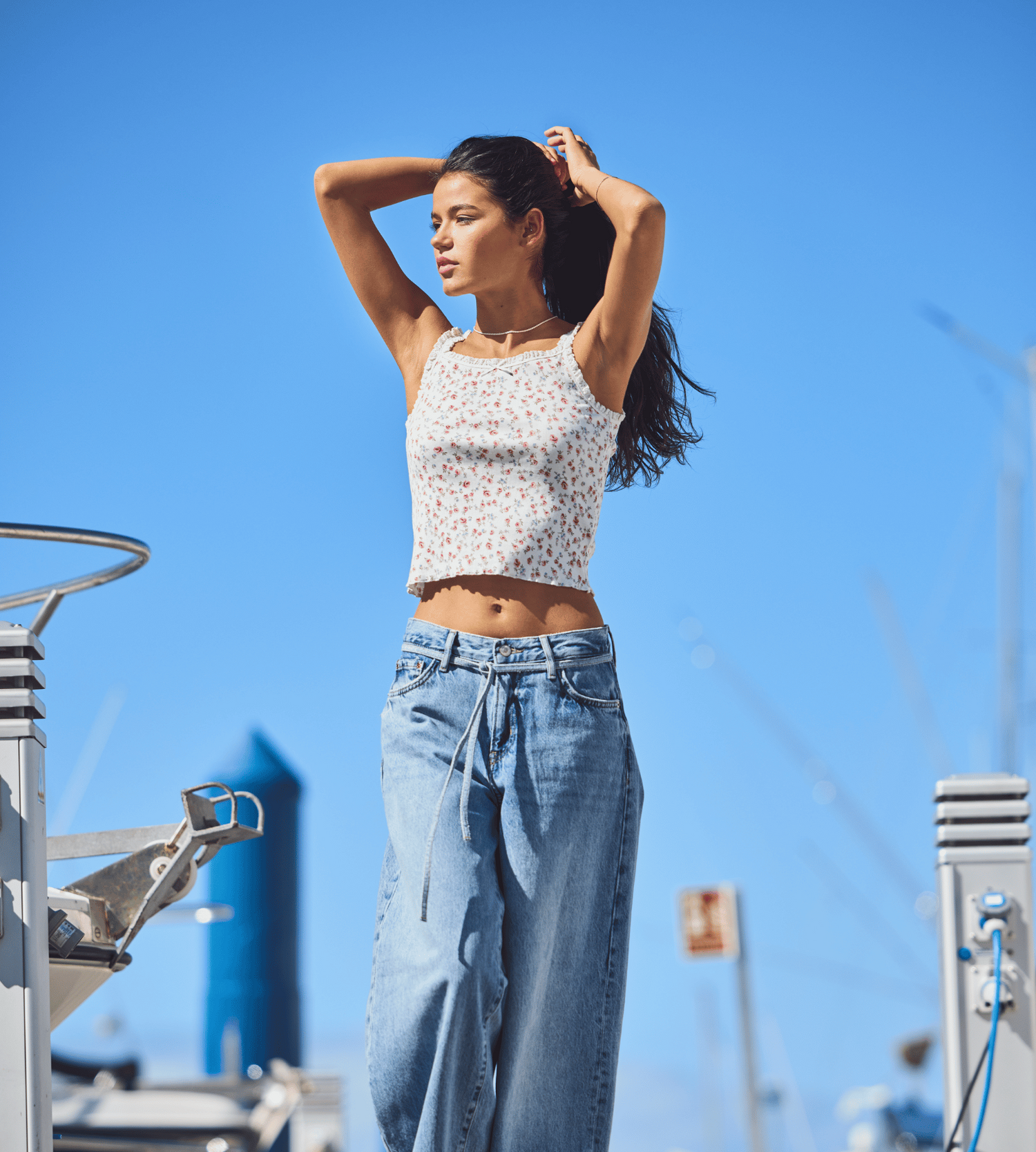 Junge Frau in Sommeroutfit steht lässig auf einem Boot – trendige Styles aus der Young Fashion Abteilung