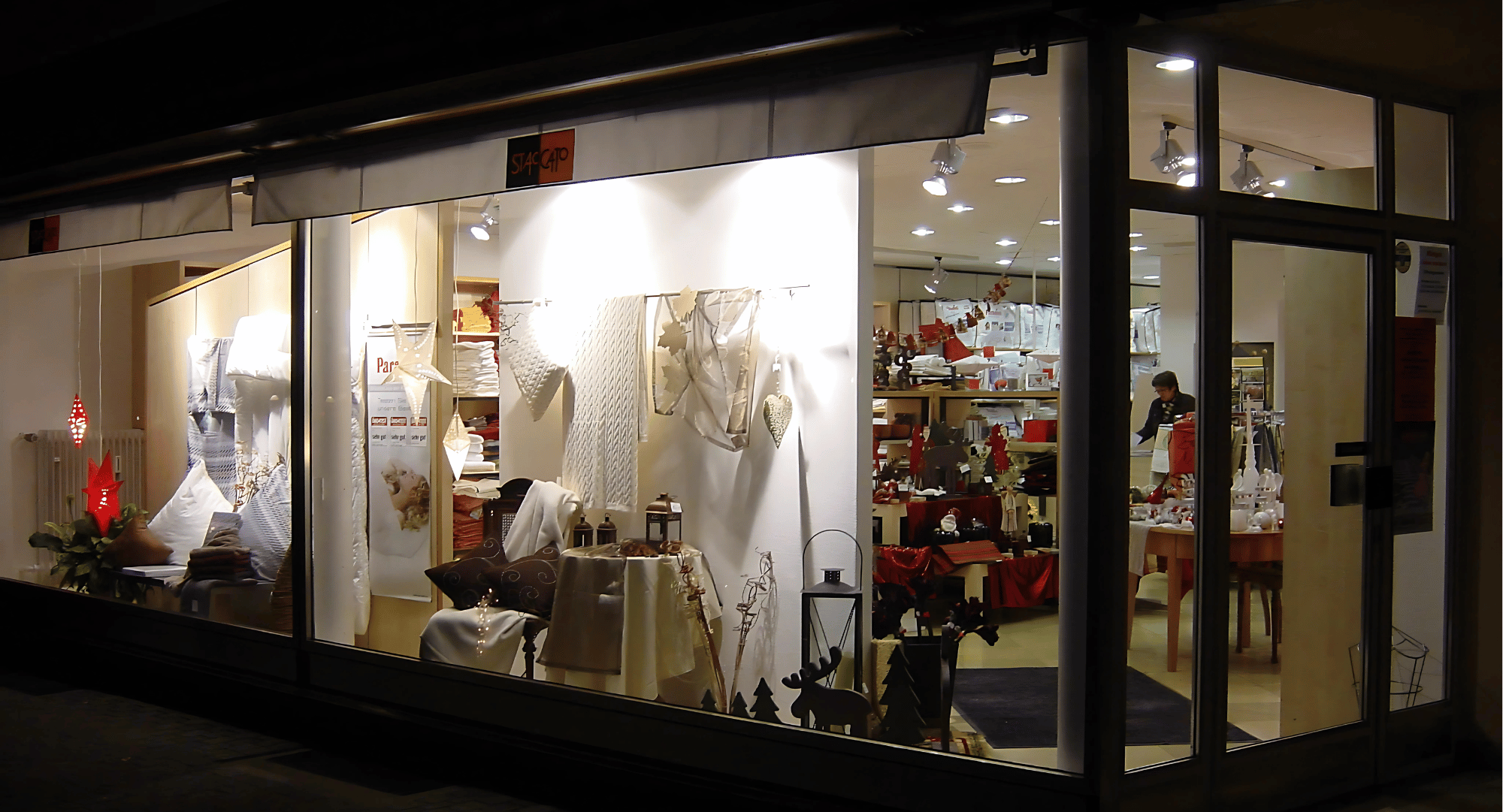 Außenansicht des Kimpel Heim & Bett Ladengeschäfts mit dekoriertem Schaufenster für Heimtextilien und Wohnaccessoires bei Nachtbeleuchtung